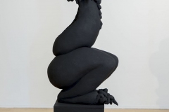 Perched female form with claw feet and bubble head, flat black.