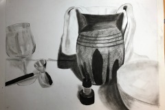 A still life on a table depicting a vase with fabric fall out of it, a wine glass, jigger, ink bottle, and bowl. The composition is high contrast, with little mid tones.