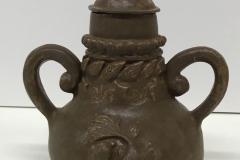 urn form with carved fish and leaves on the surface, 2 curled handles and tear drop shaped knob, glazed dark brown.