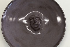 shallow bowl form with face emerging from bottom, glazed plum color.