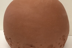 Terra cotta colored spherical jar, with crater texture at the bottom.