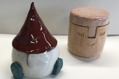 two small jars, one in the shape of a knome the other with a face carved into the surface.