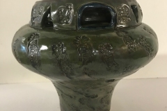 Large vase form, glazed dark green and with pressed emblems on the surface.