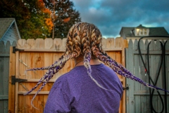 image of the back of a womans head, detailing the frozen motion of her braids flying through the air. The purple color of her hair matches her shirt.