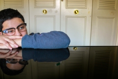 image of a man leaning his head on a highly reflective table surface.