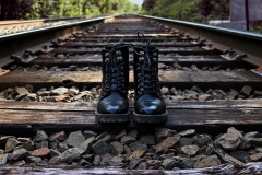 image of doc martens boots standing without a human body on the plank of a rail road track.