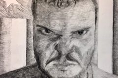 Self portrait of a man with a scowl, behind him the American flag hangs vertically.