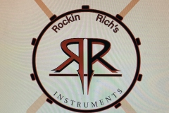 A drum with drumsticks and side by side “Rs” for Rockin Richards.