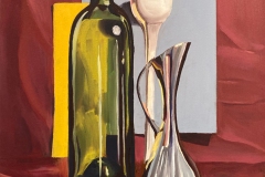 Still life of a wine bottle, tall stemmed white glass, and steel pitcher among a red fabric backdrop.
