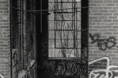 black and white image of an abandoned, graffitied building through a doorway.