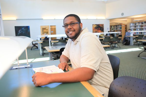 MCC student seated at table in the Library's reading room with a book.